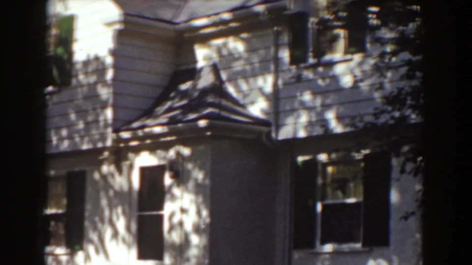 1939 New Hampshire home-movie view of a white house exterior with dark shutters, roof detail, and tree-shadow patterns.
