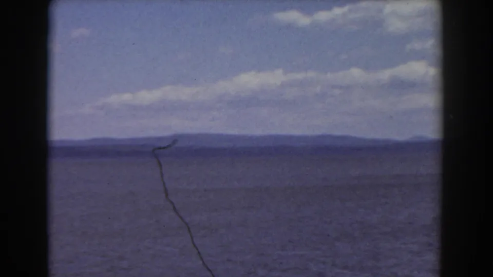 1939 Mount Washington-associated home-movie frame showing water, distant hills, and a clouded sky through dark foreground framing.