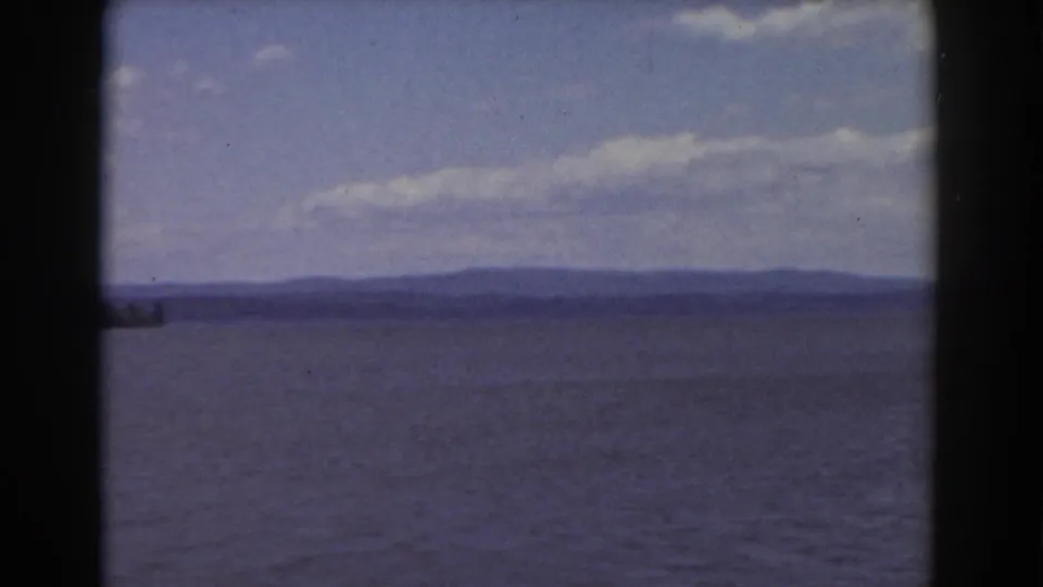 1939 New Hampshire home-movie landscape with open water, distant shoreline hills, and soft clouds in a blue sky.
