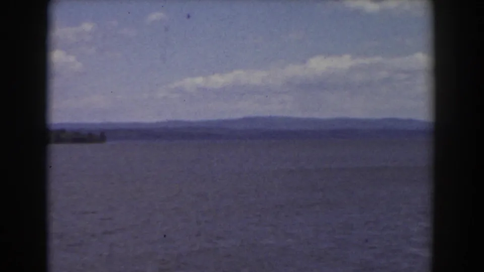 1939 Mount Washington area home-movie frame showing a broad lake, distant wooded shore, low hills, clouds, and dark 8mm borders.