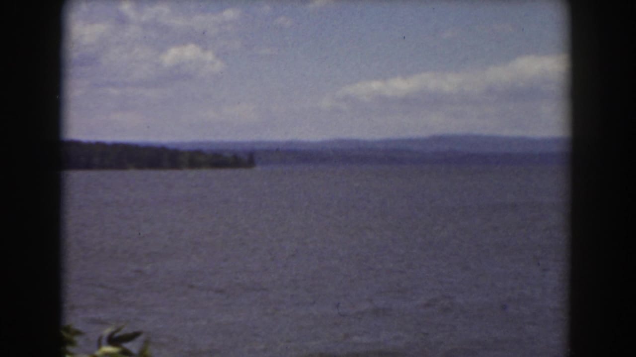 Open lake surface with a wooded point on the horizon and clouds above.