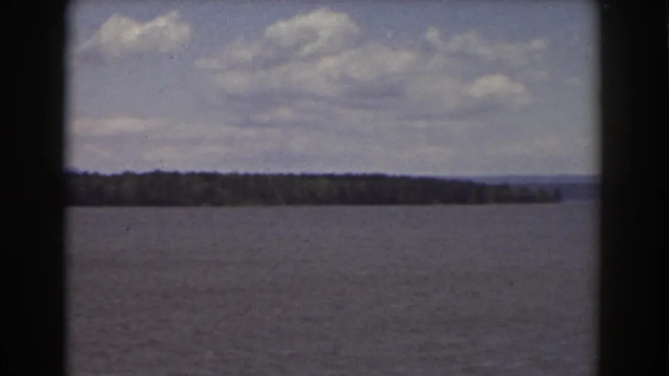 1939 8mm Mount Washington-area view across water toward a tree-lined shore and faint mountains under a partly cloudy sky.