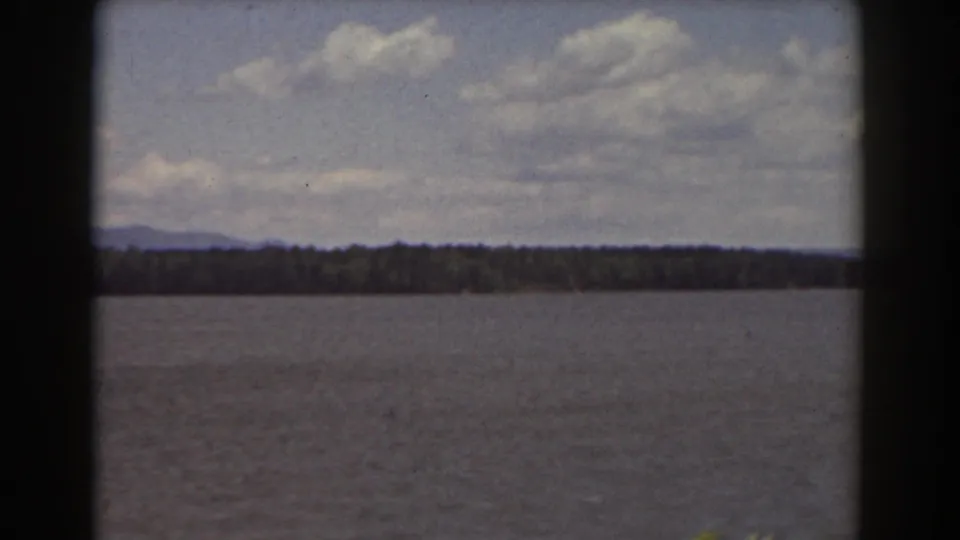 Mount Washington, New Hampshire 8mm frame showing water in the foreground, a wooded far shore, and low mountains beneath broken clouds.