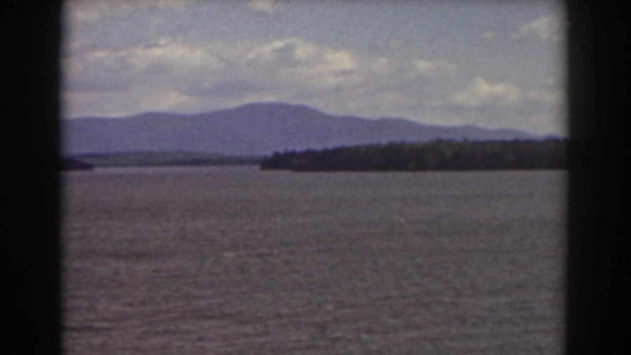 Wide lake view with a dark wooded shore and mountain ridge in the distance.