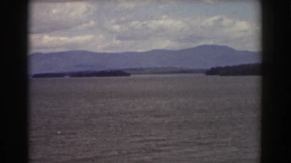 8mm Mount Washington-area landscape with open water in the foreground, layered hills beyond, and a dark shoreline to the right.