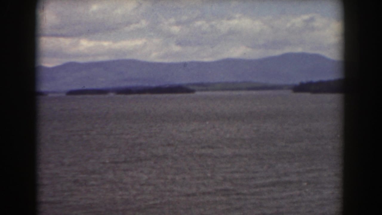 Distant mountain ridge beyond water and low wooded islands under a cloudy sky.