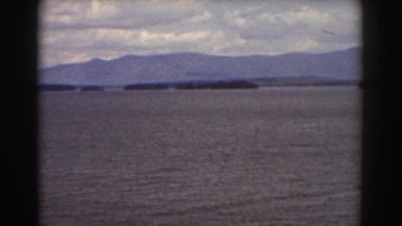 Wide water view with a dark island and blue-gray mountains beneath clouds.