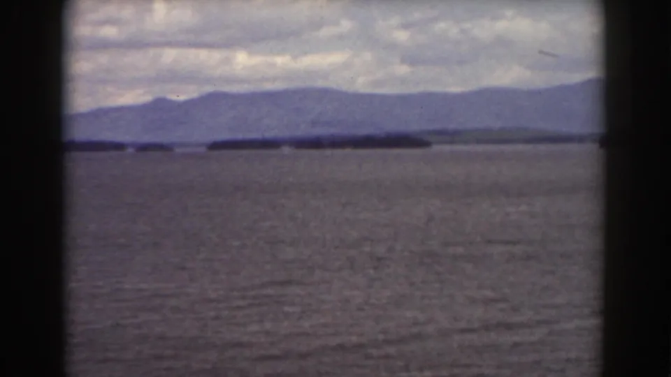 1939 Mount Washington-area view across water toward wooded islands and blue-gray mountain ridges beneath a cloudy sky.