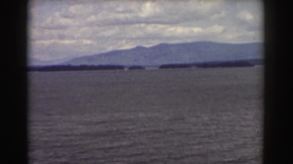 1939 Mount Washington-area home-movie frame showing water, low shoreline, and distant mountains beneath heavy clouds.