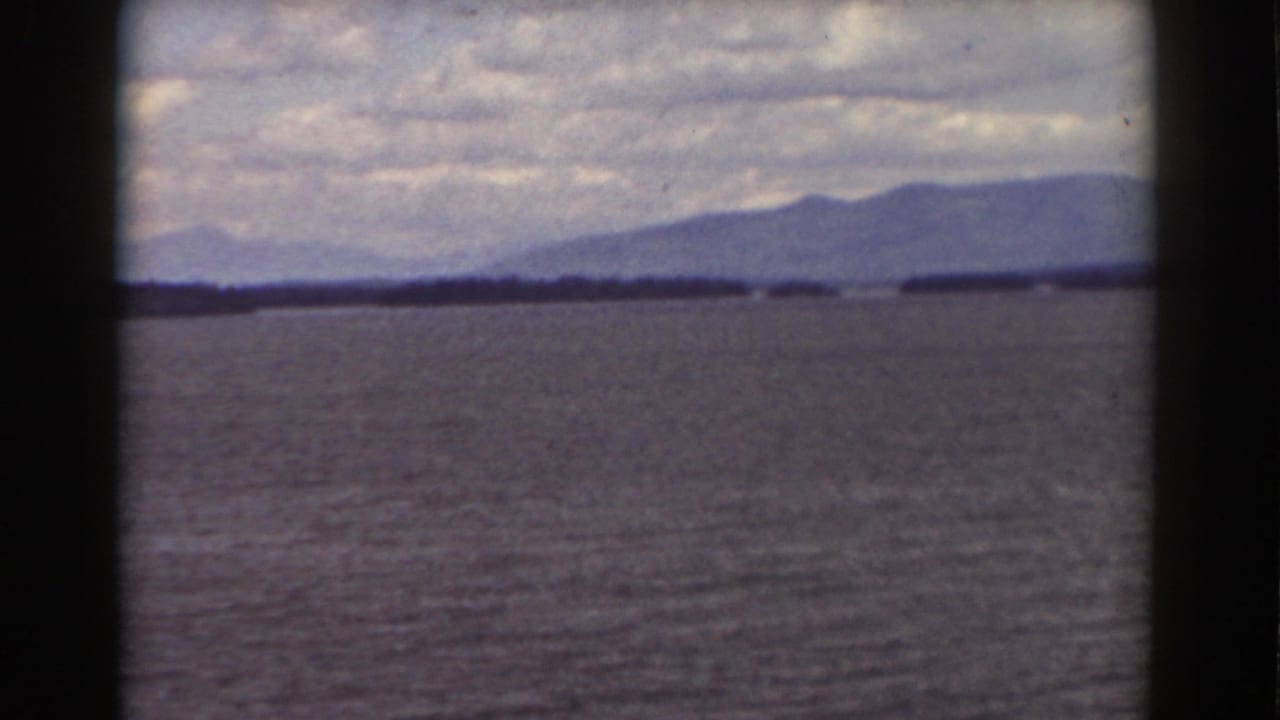 Wide water view with distant mountains and heavy cloud cover framed by dark film borders.