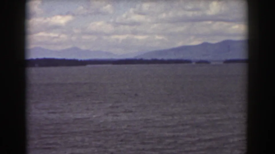 1939 home-movie landscape frame with calm water, low shoreline, and distant mountains near Mount Washington metadata.