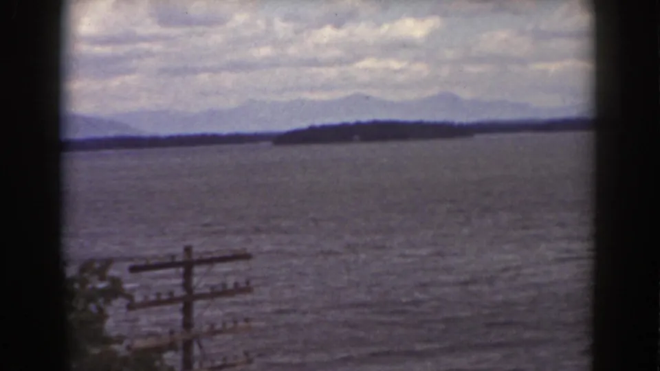 1939 8mm lakeside frame near Mount Washington with rippled water, hazy mountains, and rural utility lines.