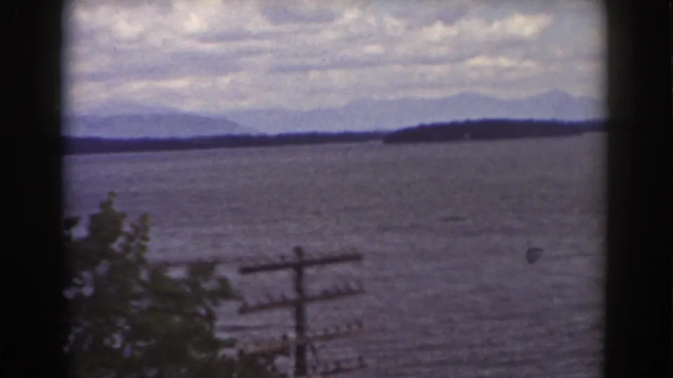 1939 Mount Washington-area lake scene framed by dark edges, with foliage, a utility pole, and distant mountains.