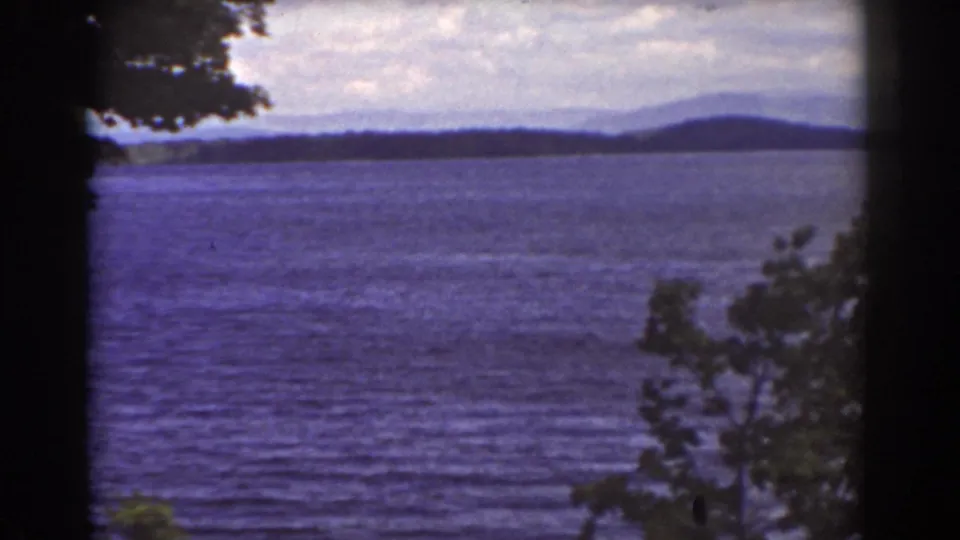 Mount Washington-area home-movie frame showing a blue lake, distant hills, and foreground tree branches during a slow pan.