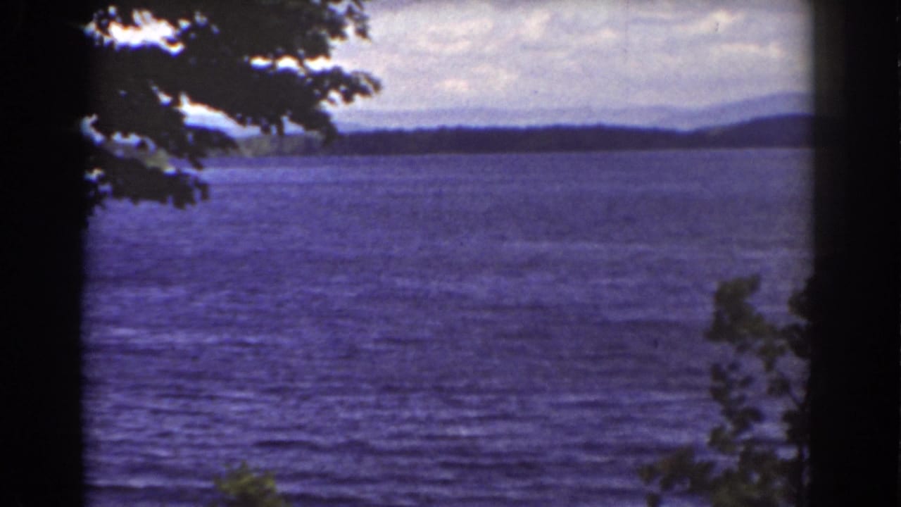 Final sampled 1939 8mm frame of the New Hampshire lake view, with rippled water, distant hills, and silhouetted tree cover.