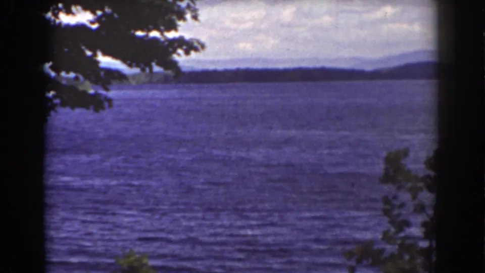 Final sampled 1939 8mm frame of the New Hampshire lake view, with rippled water, distant hills, and silhouetted tree cover.