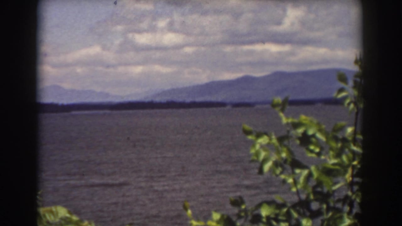 A steady 1939 home-movie frame of lake water and distant mountains near Mount Washington, with leaves entering from the right.