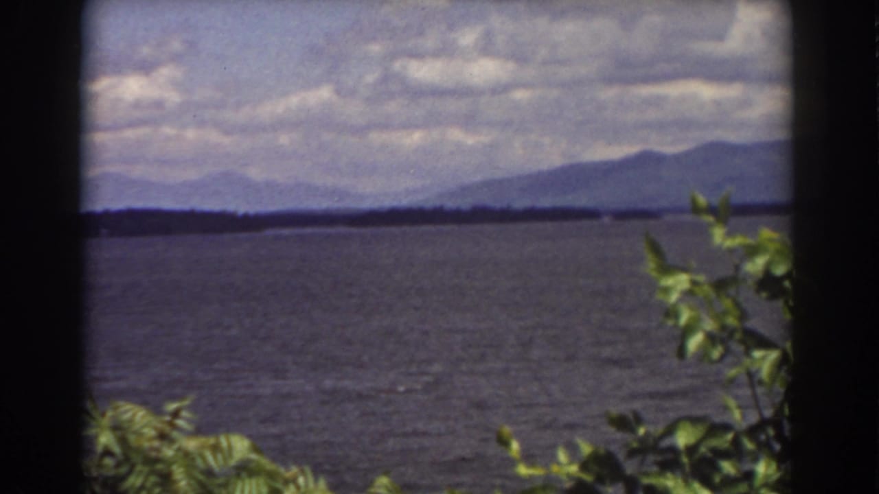 1939 8mm landscape view near Mount Washington, with rippled lake water, distant mountains, clouds, and foreground greenery.