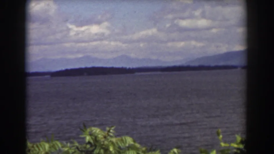 1939 8mm home-movie view near Mount Washington showing a lake, distant hills, mountain ridges, clouds, and leaves in the foreground.