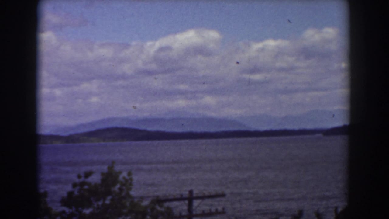 1939 Mount Washington area view across water toward hazy hills, with clouds above and foreground vegetation below.