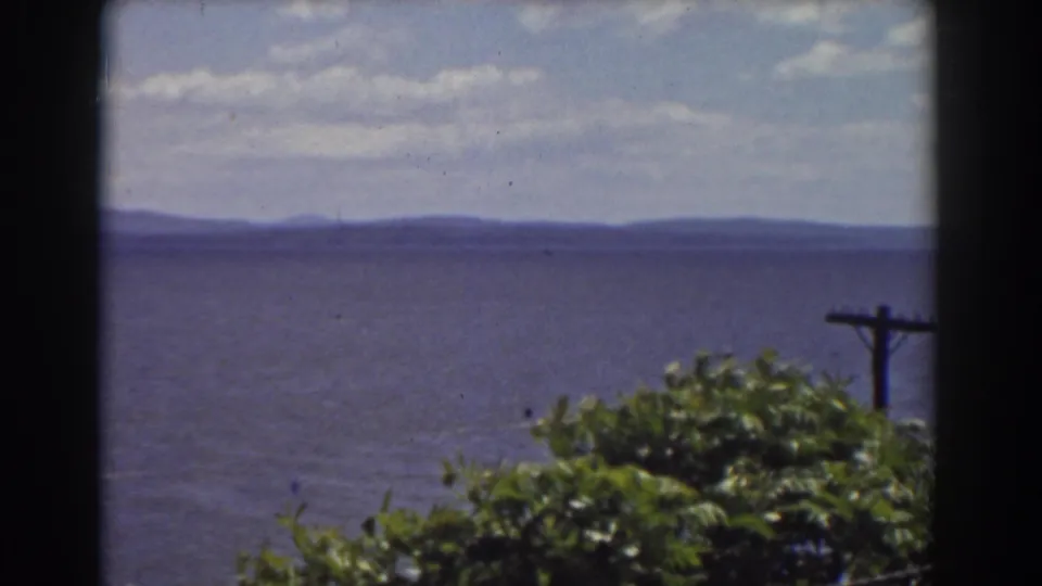 1939 Mount Washington-area home-movie view toward distant water and hills, with leaves and a dark window or frame edge in the foreground.