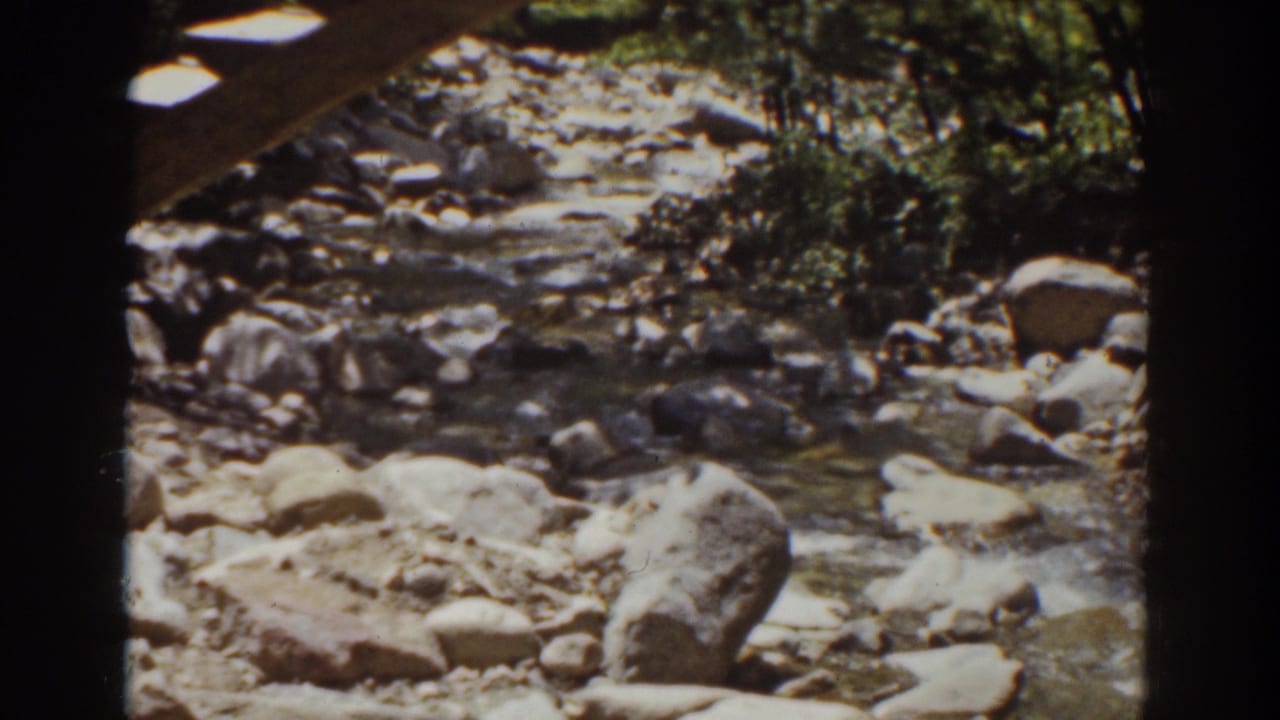 Rocky stream scene from the 1939 Mount Washington home movie, with large stones, wooded banks, and dark film borders visible.