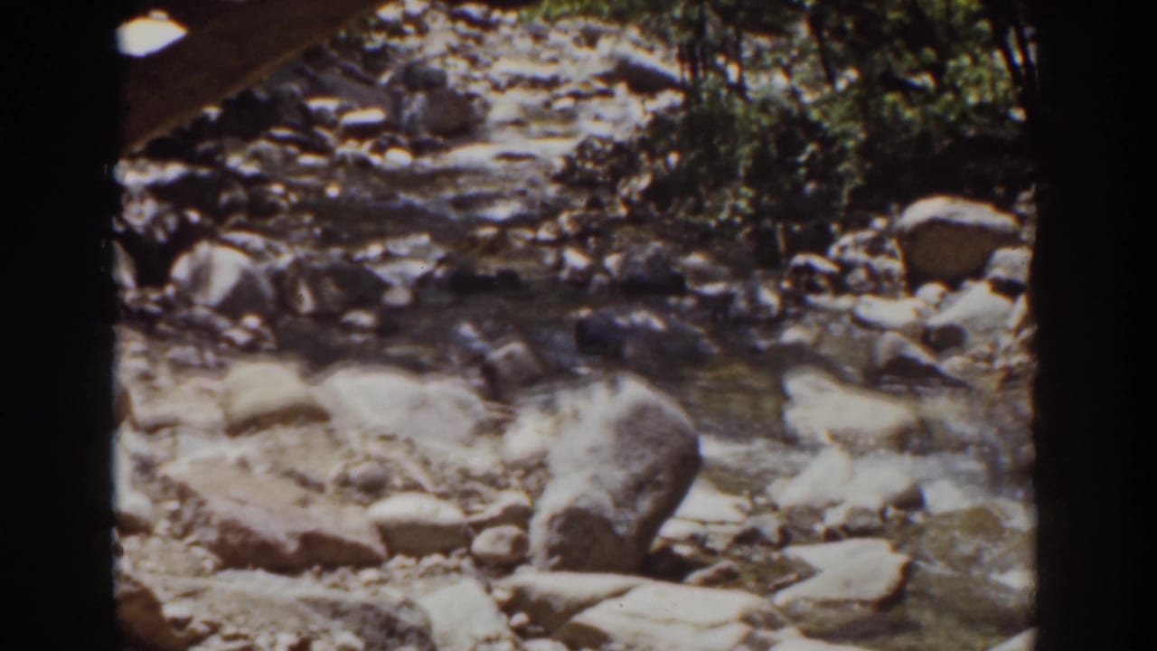 A 1939 Mount Washington home-movie frame shows a shallow rocky stream bordered by trees and sunlit stones.