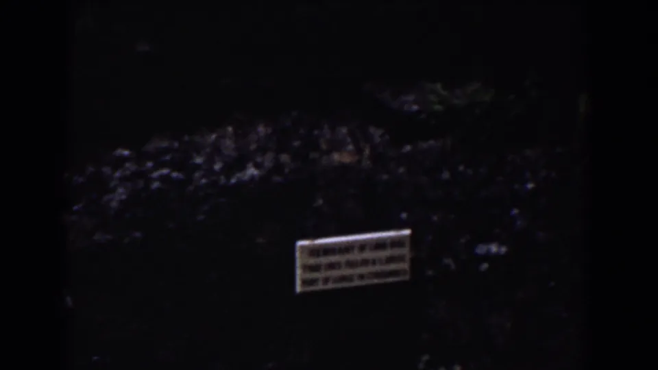 1939 Mount Washington frame with a small posted sign on a shadowed rock face beside dark water and surrounding vegetation.