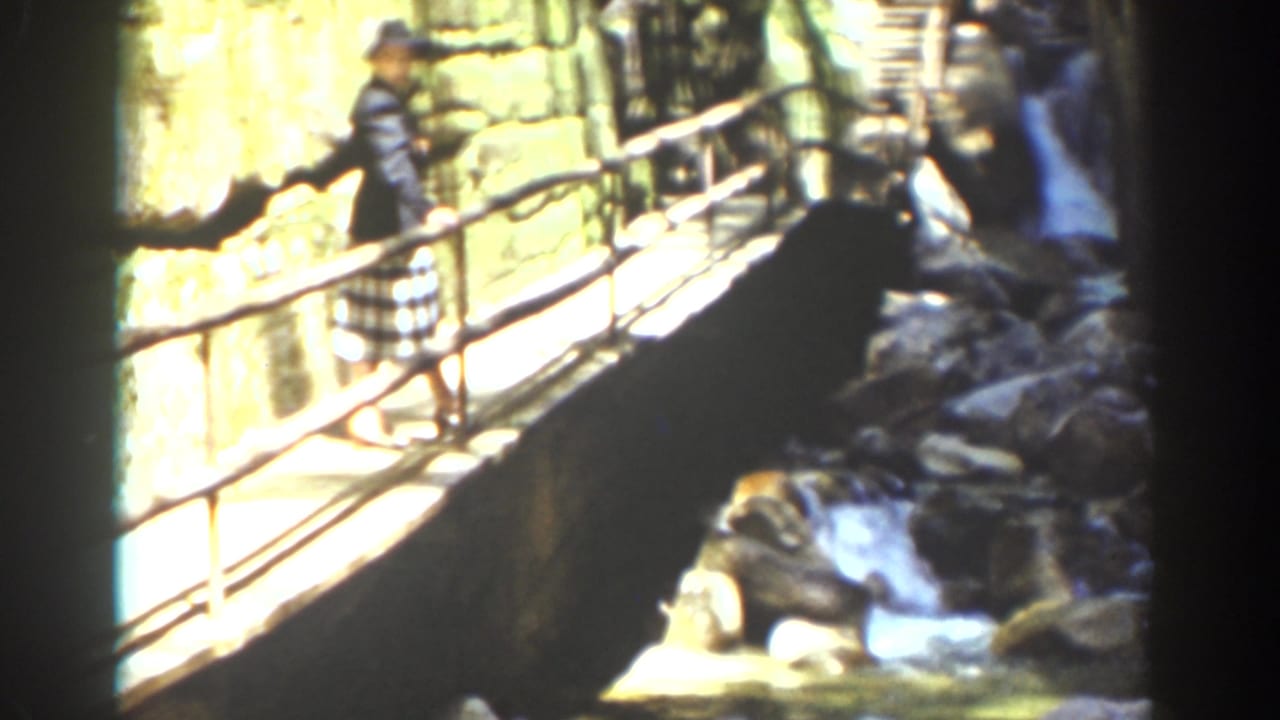 A distant visitor in period clothing crosses a wooden bridge over rocky water in the Mount Washington travel scene.