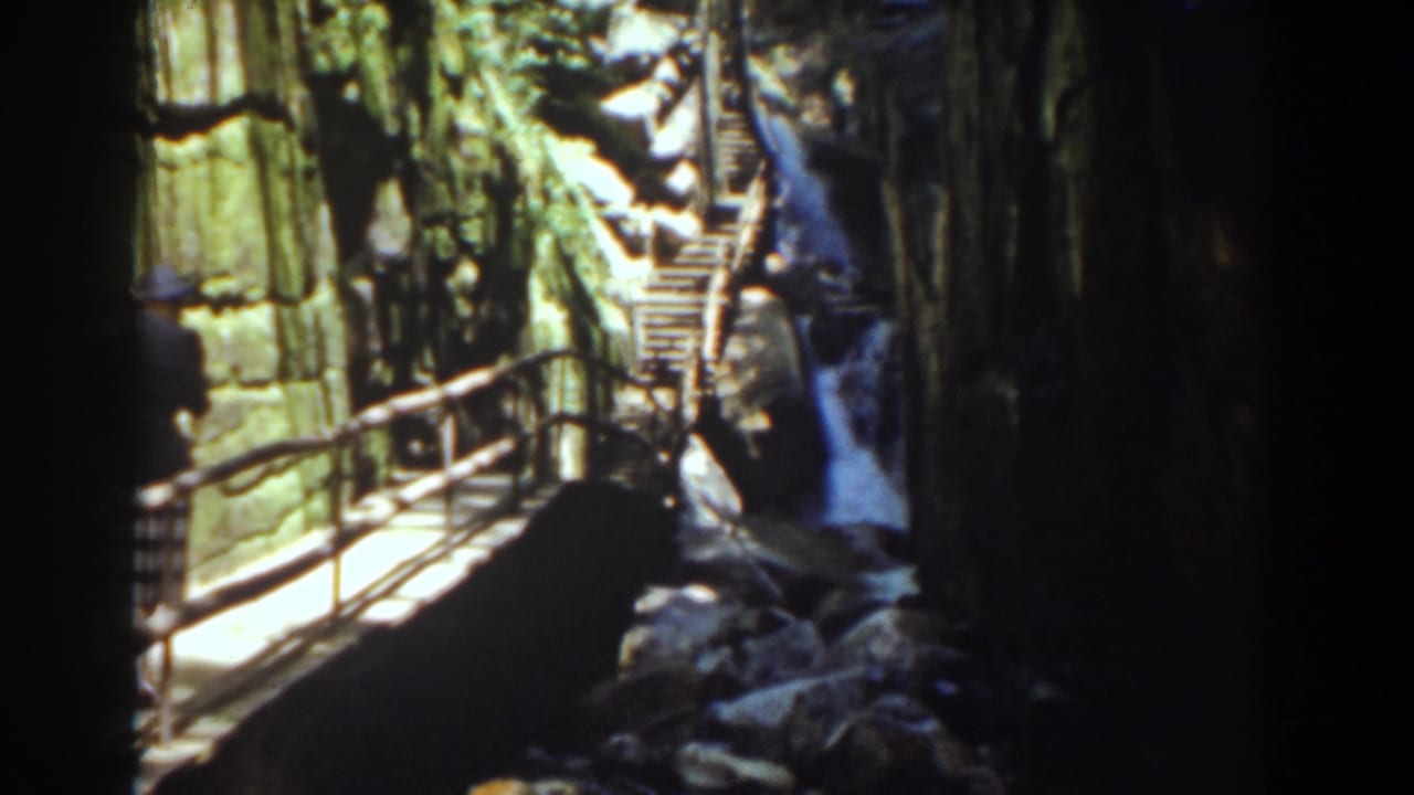 Wooden walkway and stairs beside a waterfall in a rocky gorge.