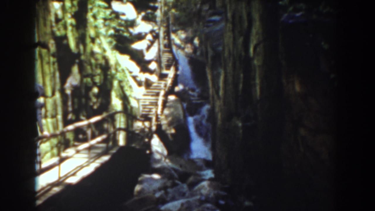 A distant visitor stands near the wooden gorge walkway as the waterfall and stairs fill the Mount Washington scene.
