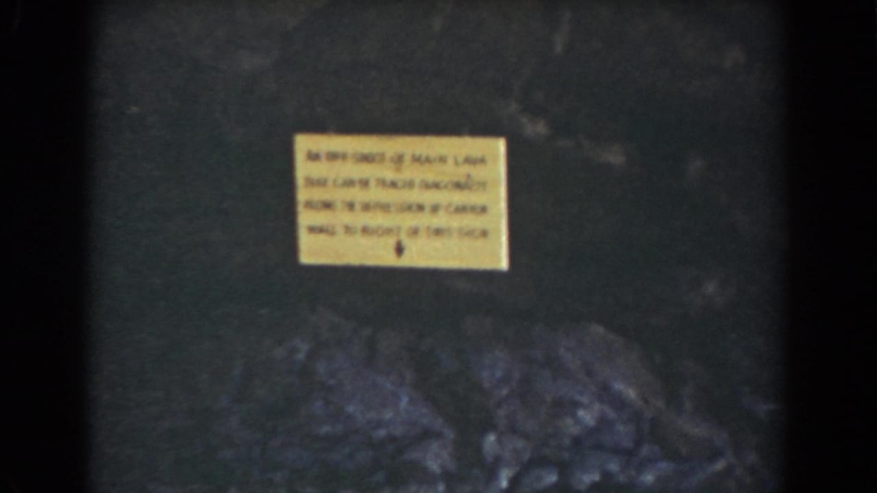 Yellow warning sign on a rock wall in the Mount Washington gorge footage, with dark stone and boulders below.