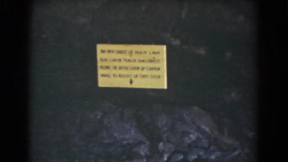 Yellow warning sign on a rock wall in the Mount Washington gorge footage, with dark stone and boulders below.
