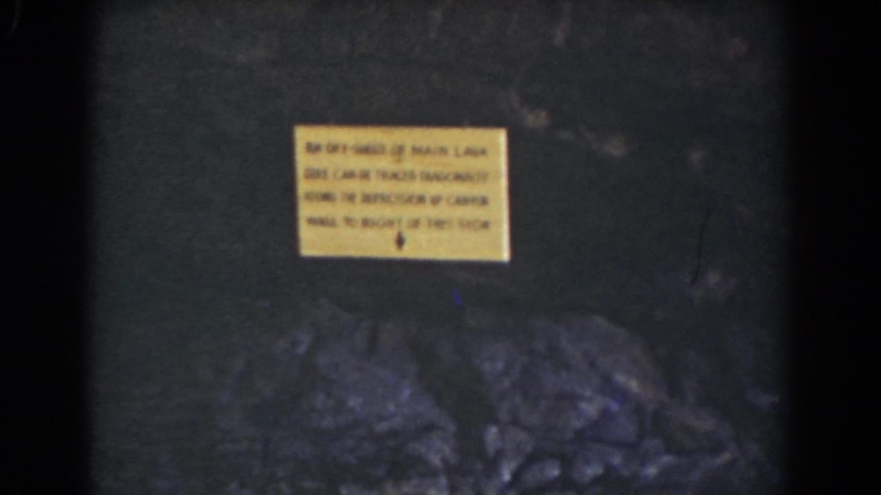 1939 Mount Washington home-movie frame showing a yellow caution sign on a dark rock face with rough stones below.