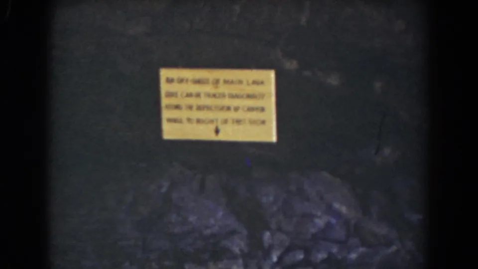1939 Mount Washington home-movie frame showing a yellow caution sign on a dark rock face with rough stones below.