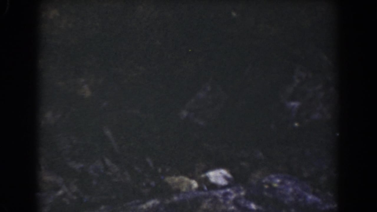 Mount Washington home-movie frame showing dark rock texture and scattered stones after the camera drops below the sign.