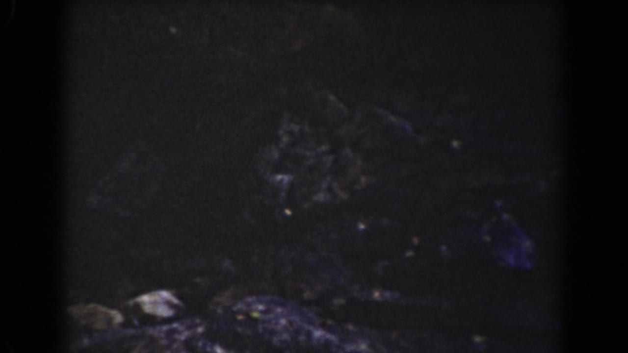 Late frame from the Mount Washington clip showing shadowed rock, rough stones, and the upper sign area mostly cropped out.