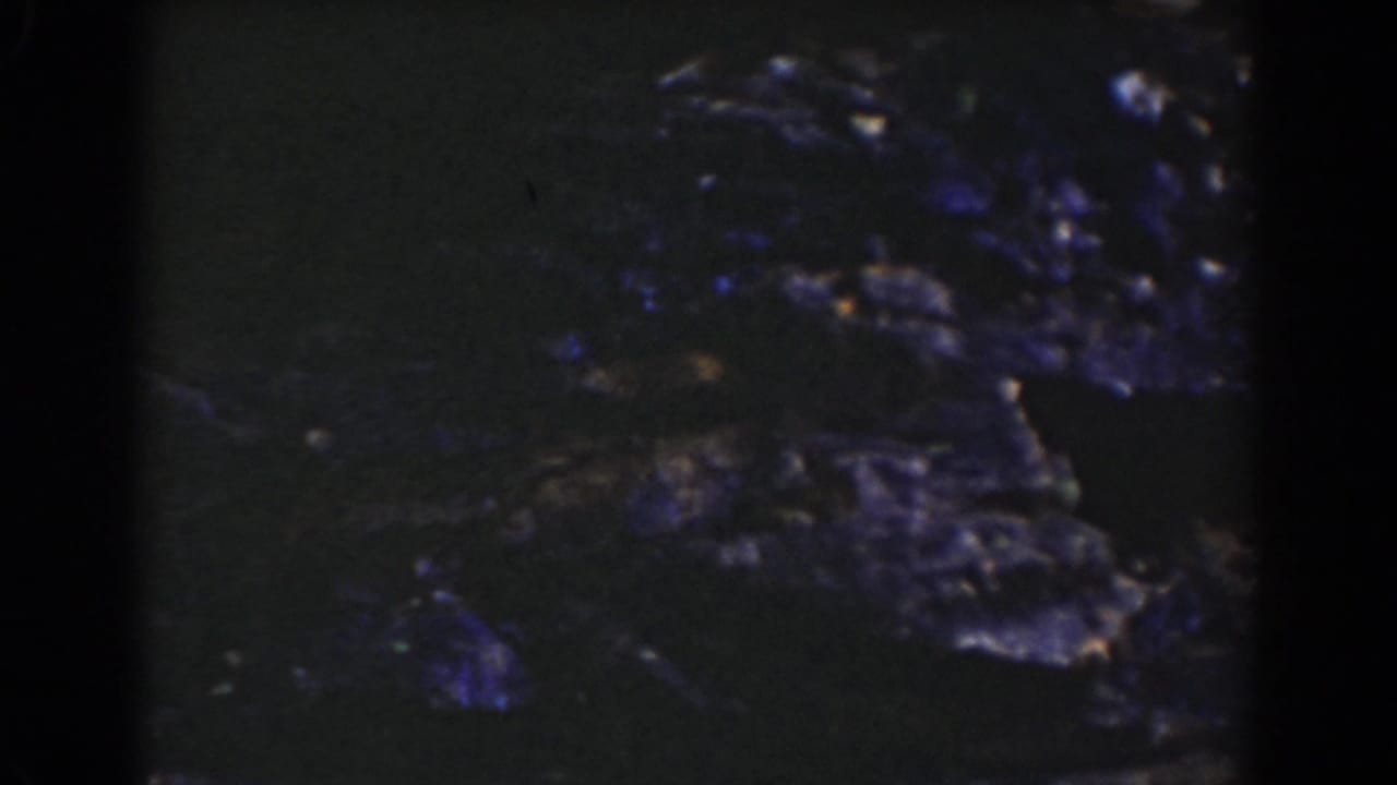 Vintage 8mm frame from Mount Washington showing dark rugged stones and small water highlights across the stream bed.