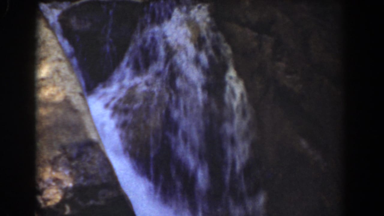 Mount Washington 1939 home-movie frame showing a narrow white cascade falling beside dark stone in a shaded mountain setting.