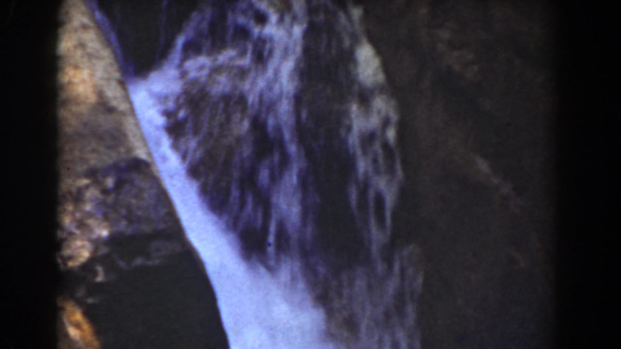 Pale water flows down dark rock in a close-up waterfall view.