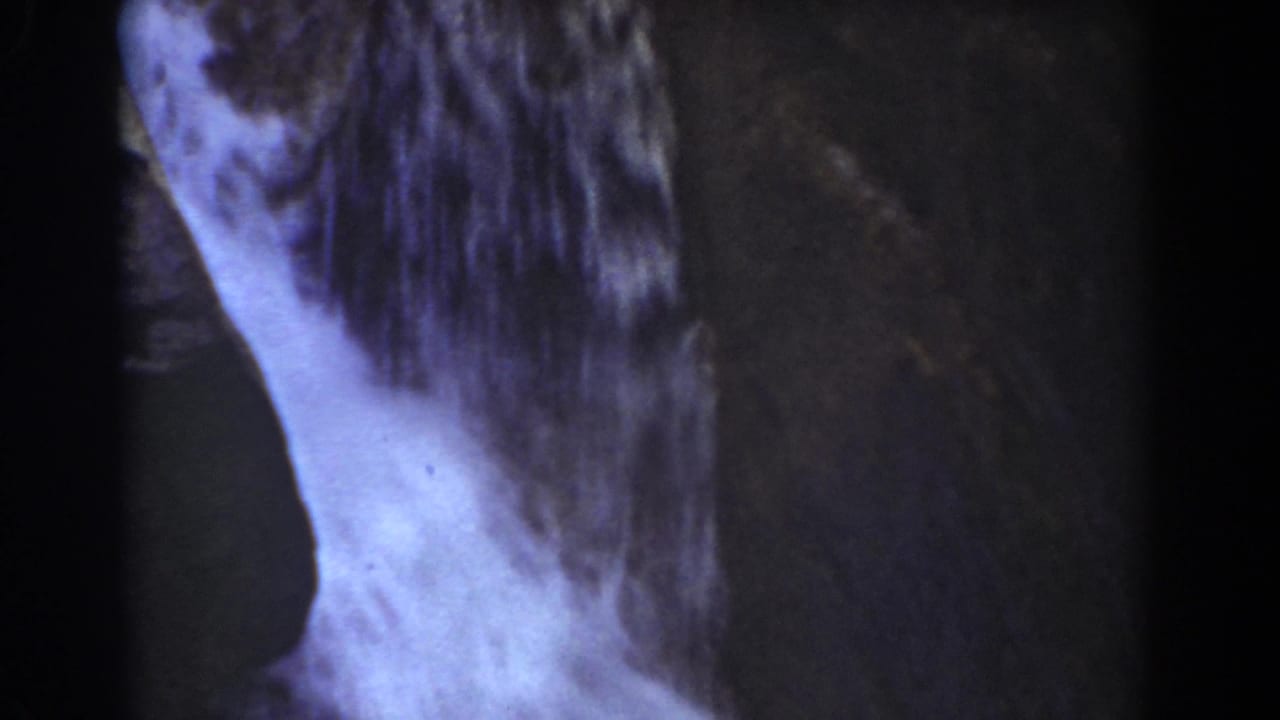 Narrow sheet of water descends beside a dark rock face.