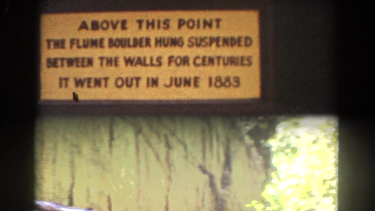 The camera frames the Flume Boulder plaque with rough stonework and sunlit foliage below in New Hampshire travel footage.