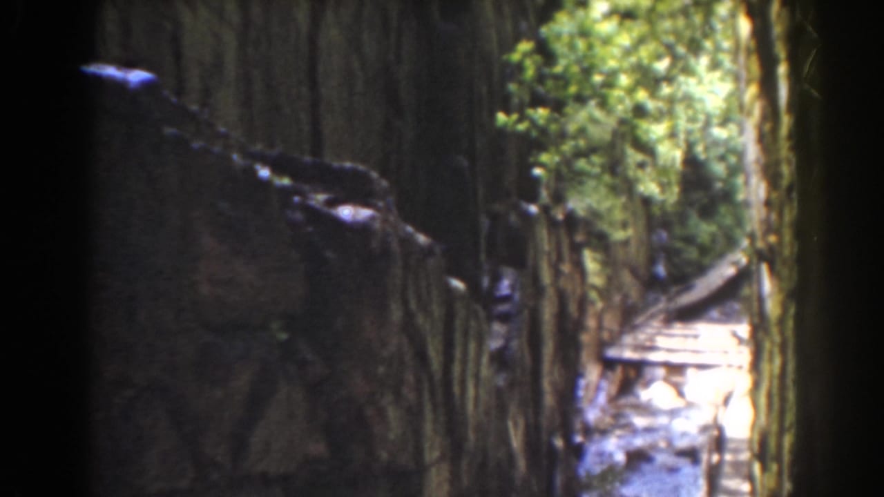 1939 Mount Washington home-movie view of a narrow forest channel with textured walls and bright water or walkway in the distance.