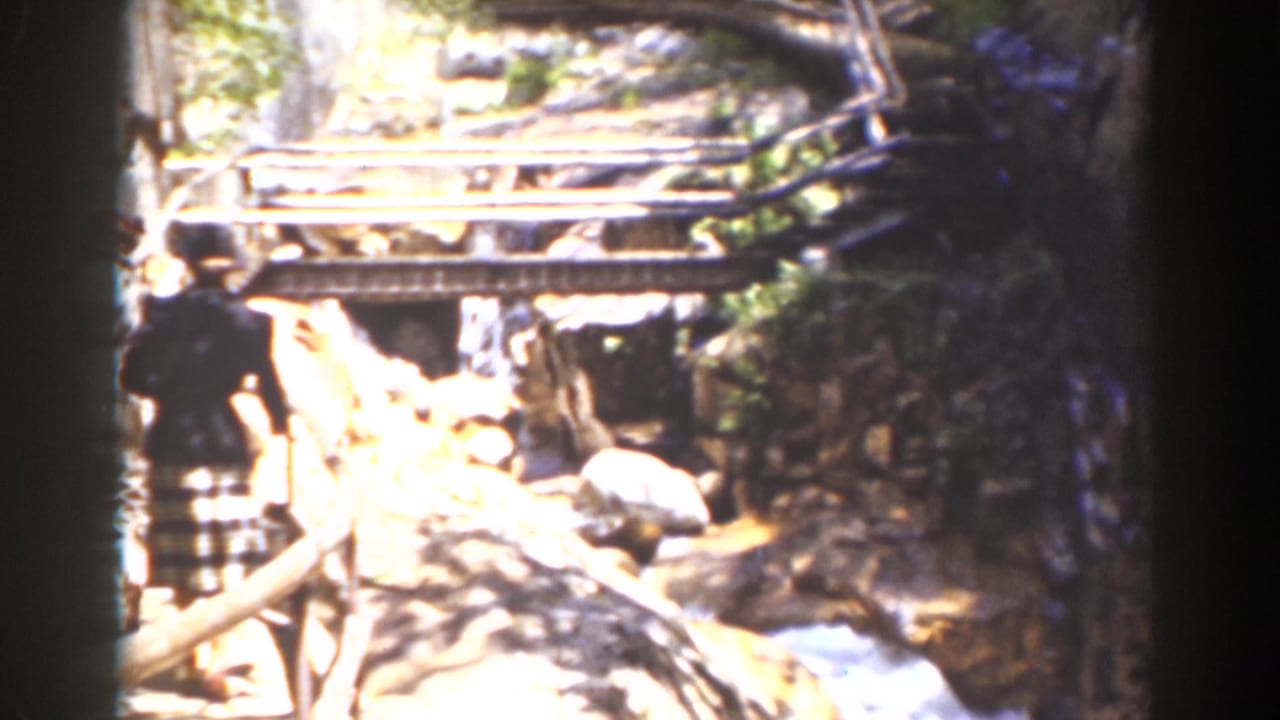 1939 Mount Washington frame showing a timber bridge over a rocky stream, with a distant pedestrian along the left path.