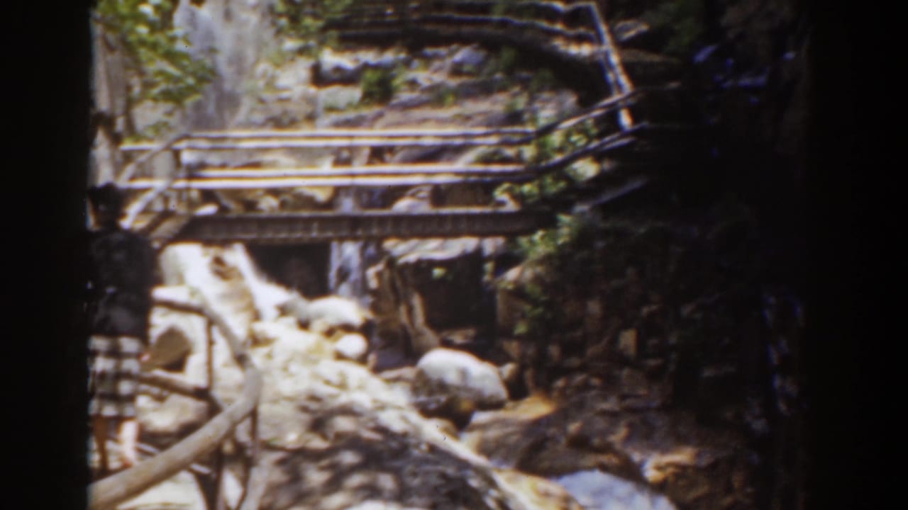 Mount Washington 8mm frame of a rustic wooden bridge crossing a bright rocky stream between steep, wooded rock walls.