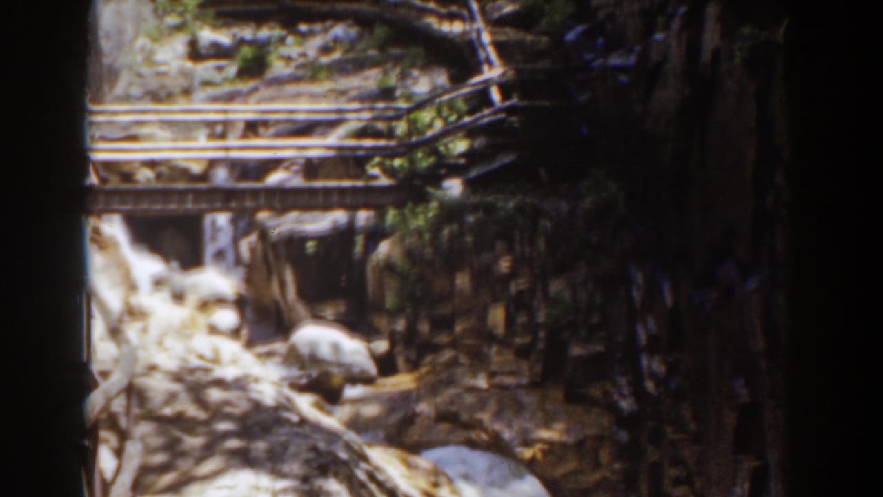 1939 Mount Washington 8mm frame with a wooden footbridge, boulders, and water running through a forested rocky channel.