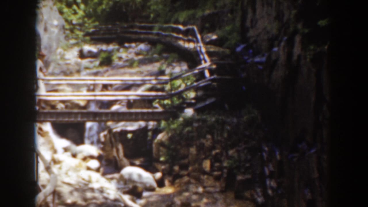 Mount Washington home-movie view of a rustic bridge and rocky stream, with wooded slopes and uneven handheld framing.