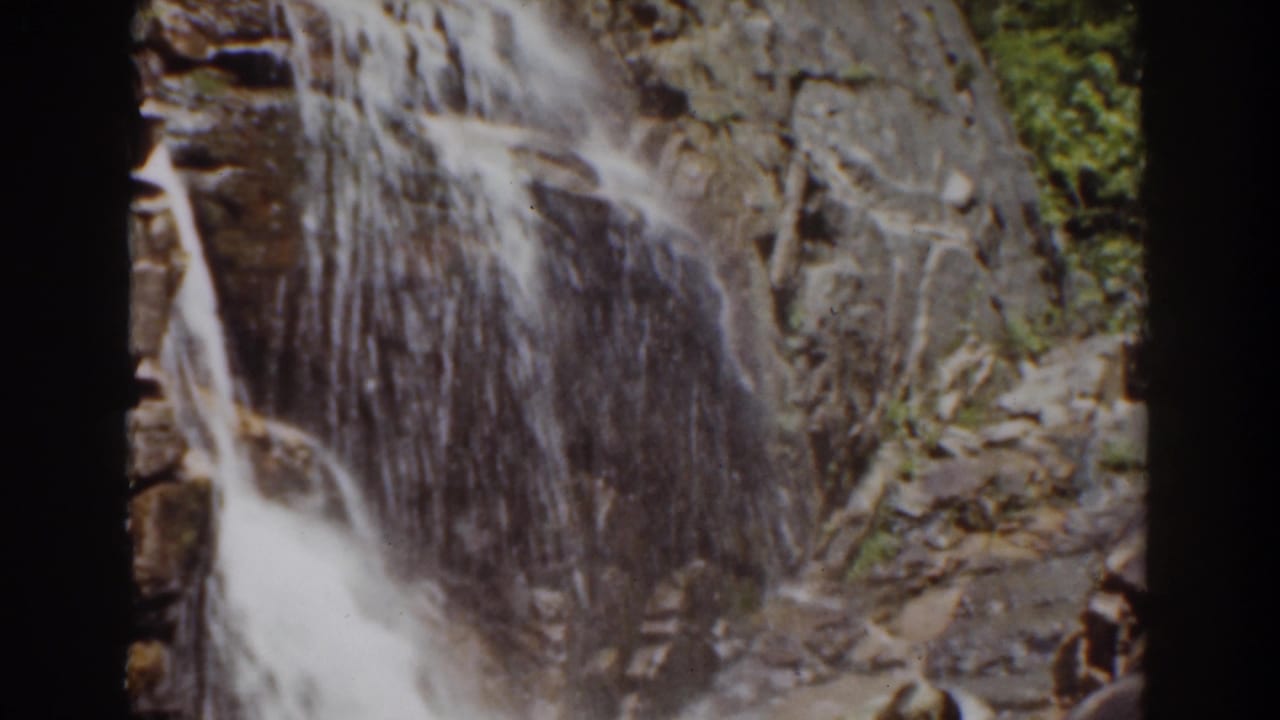 1939 8mm Mount Washington footage showing a waterfall cascading down a rugged rock face with green trees at the side.