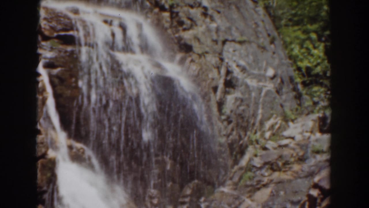 A New Hampshire mountain waterfall breaks into several streams over dark, textured rock in this 1939 home-movie frame.