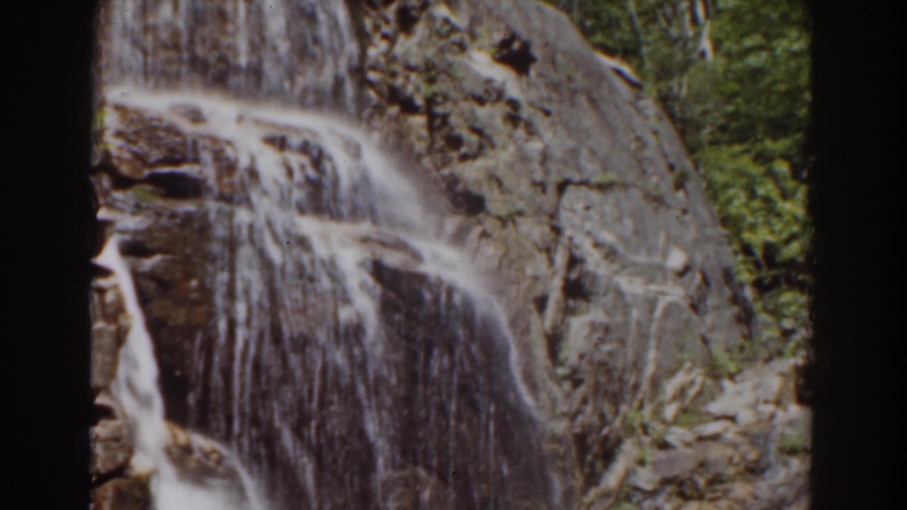 The 8mm frame holds on frothy water spilling down a steep rock surface, with foliage partly visible at the right edge.
